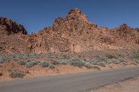 a motorcycle traveling down a desert road past some rocky cliffs under a blue sky and blue sky