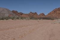 a desert area with dirt road and rocky mountains in the background and a blue sky