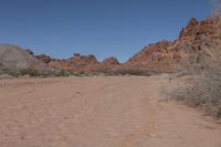 a desert area with dirt road and rocky mountains in the background and a blue sky