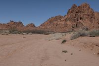 a desert area with dirt road and rocky mountains in the background and a blue sky