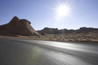 sun shining over the desert and rocky hill behind a motorcycle rider on an all road highway