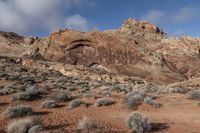 a view of a red rock and rocky landscape in the mountains near an area with bushes and sparse brush