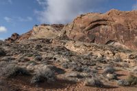 a view of a red rock and rocky landscape in the mountains near an area with bushes and sparse brush