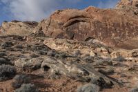 a view of a red rock and rocky landscape in the mountains near an area with bushes and sparse brush