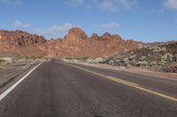 a motorcycle is shown riding on an empty road in the desert near mountains and cliffs