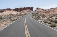 the empty road is lined by bushes and rocky mountain peaks in the desert area of moab