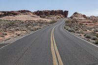 the empty road is lined by bushes and rocky mountain peaks in the desert area of moab