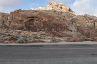 a man riding a motorcycle down the middle of a road with big mountains in the background