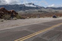 the road is lined with rocks, bushes and dirt mountains are visible in the background