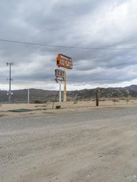 two motel signs near an old gas station in the desert area of california, one with a large red fire hydrant in the middle of the road