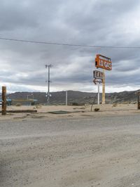 two motel signs near an old gas station in the desert area of california, one with a large red fire hydrant in the middle of the road