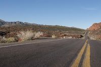 road between red hills and desert with a yellow strip in the middle of it that marks the path to the left