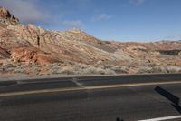 a red rock is in the distance behind a street sign and hills and clouds in the blue sky