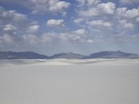snow in the middle of a vast plain with mountains in the distance and a cloudy blue sky