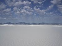 snow in the middle of a vast plain with mountains in the distance and a cloudy blue sky