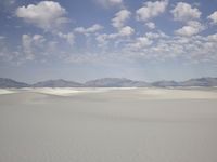 snow in the middle of a vast plain with mountains in the distance and a cloudy blue sky