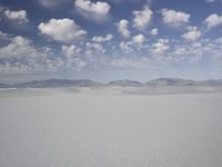 snow in the middle of a vast plain with mountains in the distance and a cloudy blue sky