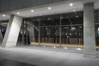 the large, open building is illuminated at night time by low flood lights and concrete columns