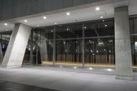 the large, open building is illuminated at night time by low flood lights and concrete columns