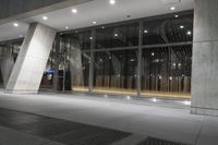 the large, open building is illuminated at night time by low flood lights and concrete columns