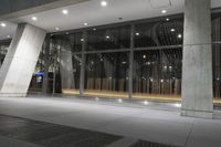 the large, open building is illuminated at night time by low flood lights and concrete columns