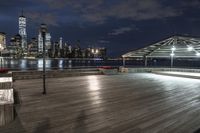 a view of new york city skyline at night from pier on the hudson river side