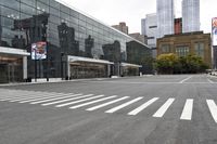 a cross walk in front of a glass building with skyscrapers in the background and one white dotted on the street