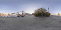 an empty parking lot on the side of the river with a bridge over it and buildings in the background