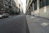 an empty road is surrounded by tall buildings on both sides with parked cars in the street