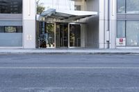 an entrance into a glass building and street scene on a gray day with blue sky and clouds