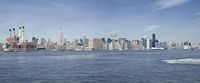 the lower manhattan buildings are on the horizon of a city lake with boats passing by