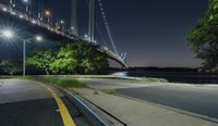 a man skateboarding on the street next to a body of water at night near a bridge