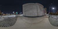 a building with no roof on the corner of a road at night as seen through the fish eye lens