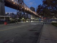 a paved road with buildings and bridge at night behind it in front of trees, in the distance,