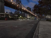 a paved road with buildings and bridge at night behind it in front of trees, in the distance,