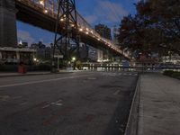 a paved road with buildings and bridge at night behind it in front of trees, in the distance,