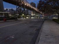 a paved road with buildings and bridge at night behind it in front of trees, in the distance,
