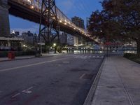 a paved road with buildings and bridge at night behind it in front of trees, in the distance,