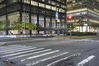 a cross walk and road in front of an office building at night with lights on