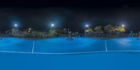 a blue tennis court and street lights lit by street lights at night in a city