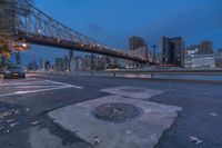 an empty road has fallen leaves and some lights on a bridge in the background in downtown pittsburgh