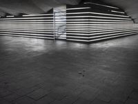 an empty open air hallway with a tiled floor, and large, vertical panels of lights