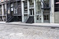 a person standing by some fire hydrants on a street near buildings and stairs and brick pavement