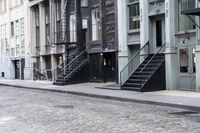 a person standing by some fire hydrants on a street near buildings and stairs and brick pavement