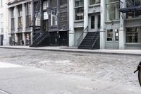 a person standing by some fire hydrants on a street near buildings and stairs and brick pavement