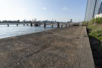 the view of a city skyline from an open river bank with a bridge and benches at the edge