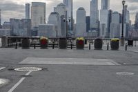 a paved park with benches next to a water body and a skyline of high rises in the background