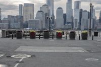 a paved park with benches next to a water body and a skyline of high rises in the background