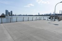 the woman is walking down the sidewalk towards the water next to her bicycle racket