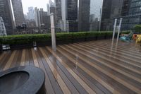 a wooden deck with metal bars and furniture in the rain over skyscrapers in the background